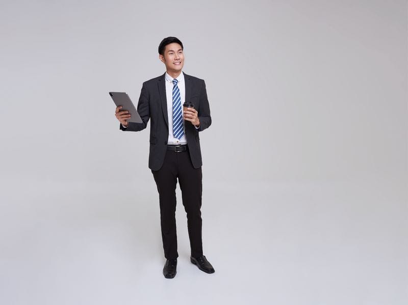 Man holds coffee cup in one hand and laptop in other smiling