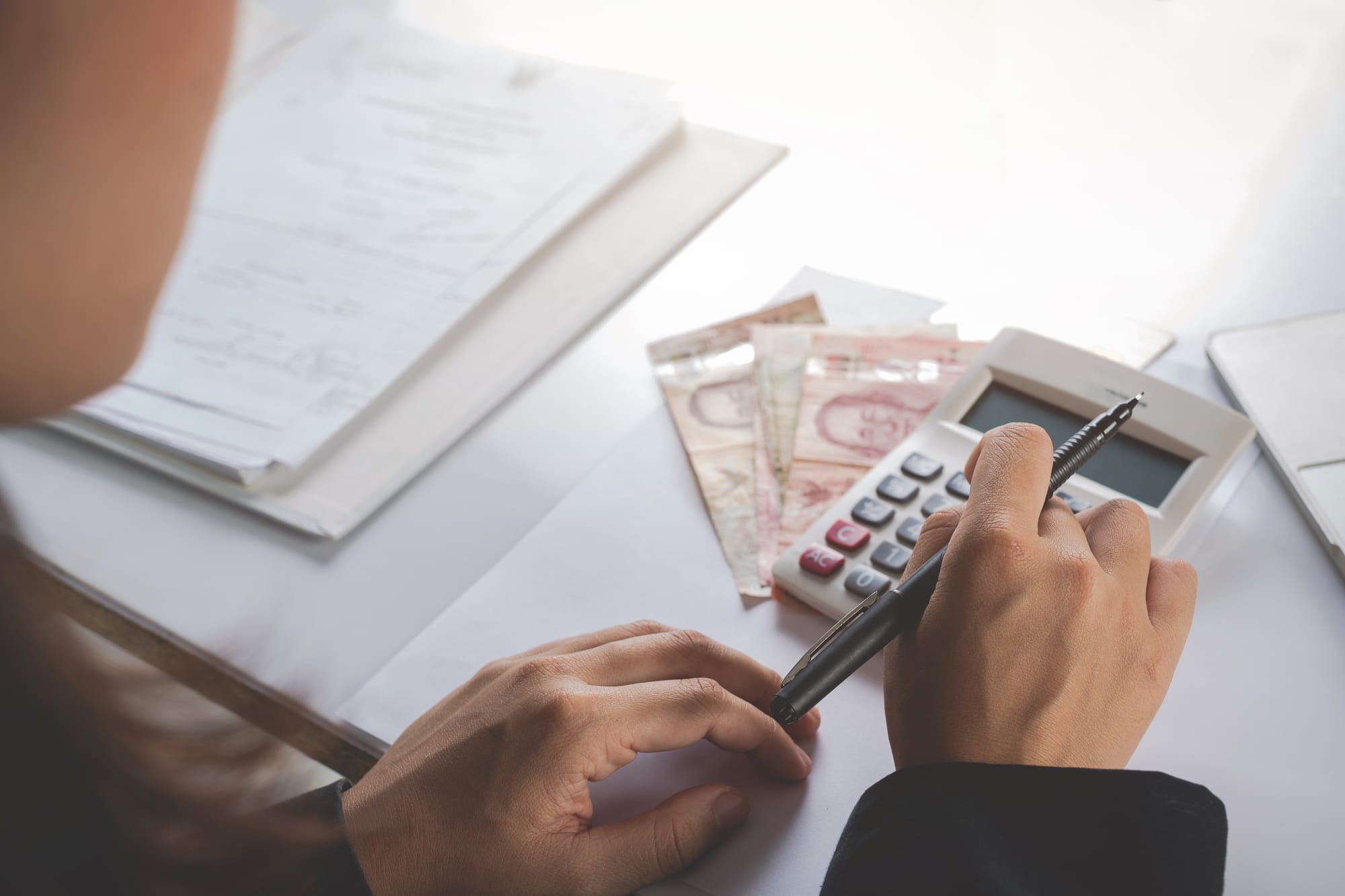 Woman typing on calculator with Thai currency on the desk