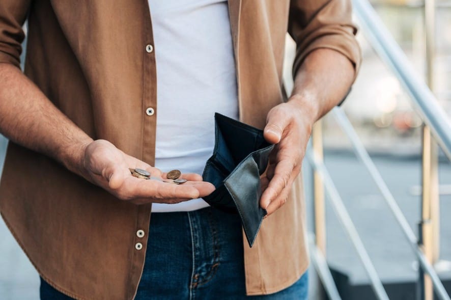 A man shows an empty wallet in one hand with coins on the other 