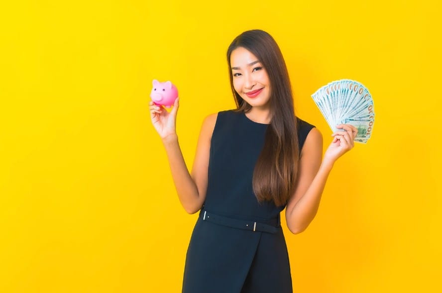 Woman holding bank notes in one hand and a piggy bank in the other