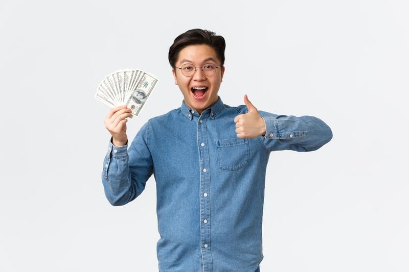 Man holding currency in one hand with thumbs up. 