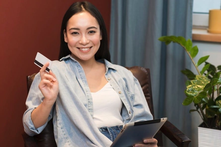 Woman holding credit card and smiling with digital tablet on hand.